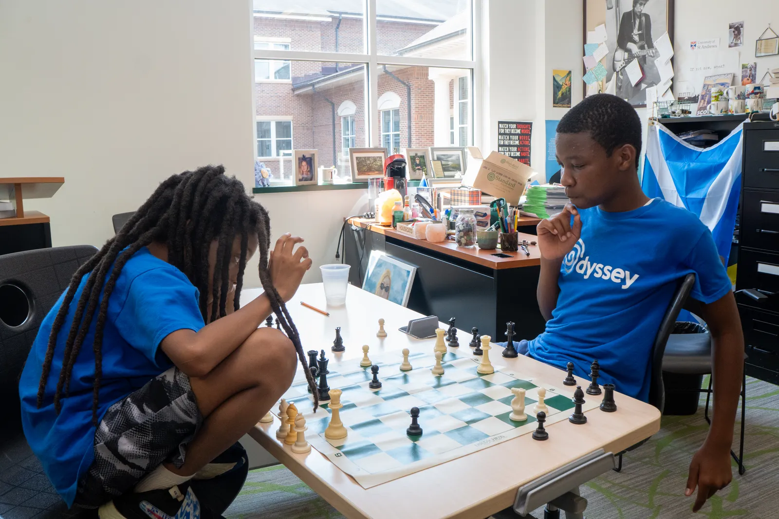 A Checkmate Your Summer student in an Odyssey shirt studying the board mid-game.