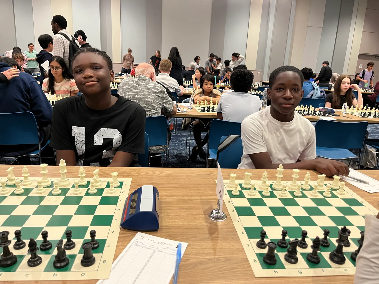 Two Rule the Board scholars at their boards at the Emory Castle Chess Grand Prix, clocks and scoresheets set up.